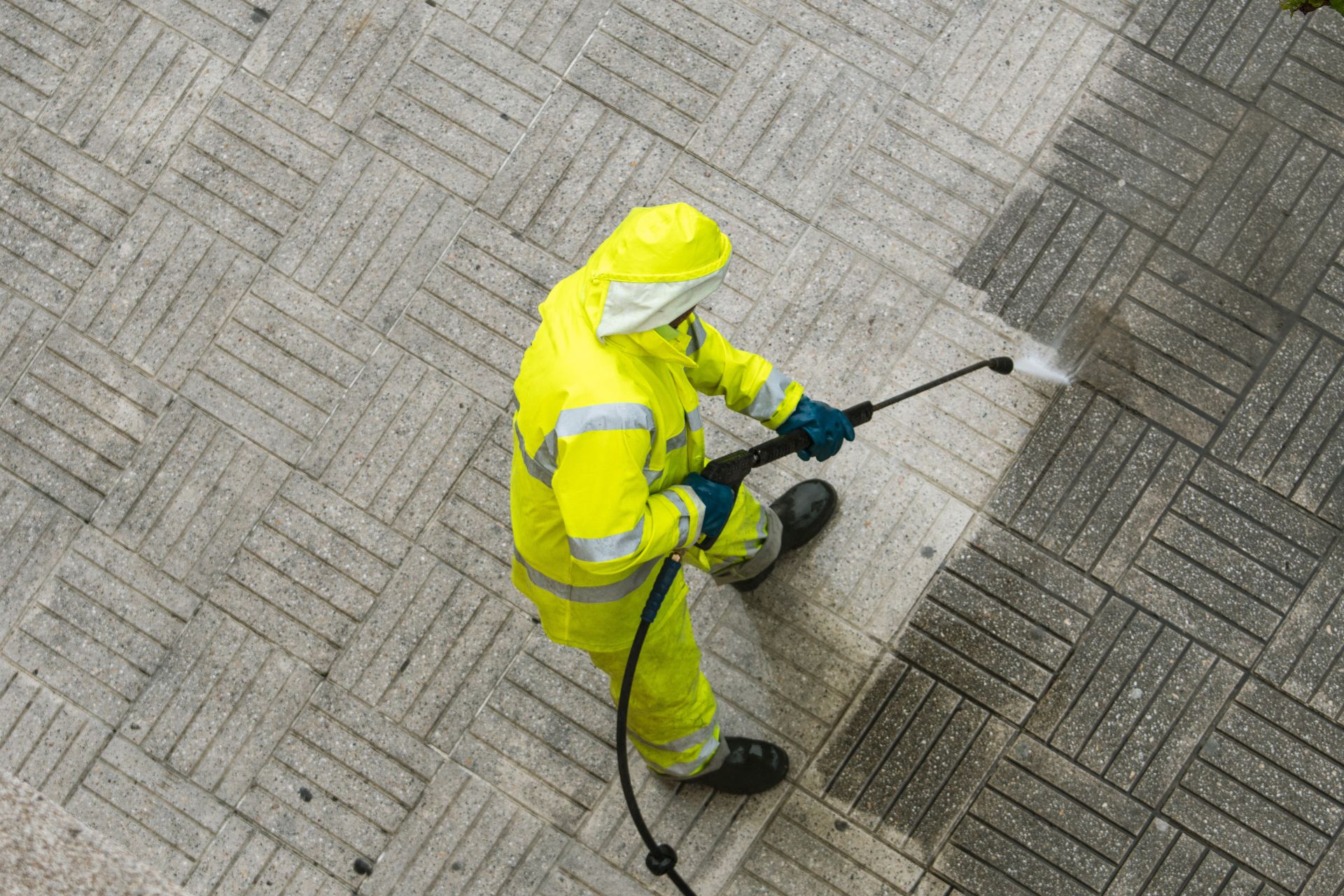 A man in a yellow suit is spraying a hose on a sidewalk.