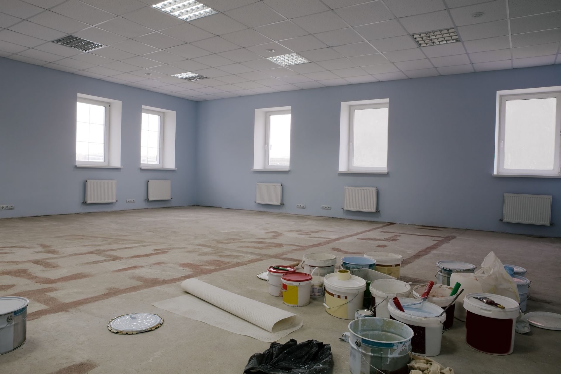 An empty room with buckets of paint on the floor.