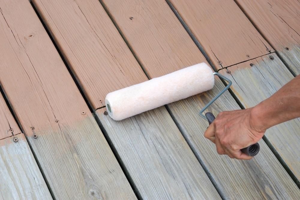 A person is painting a wooden deck with a roller.