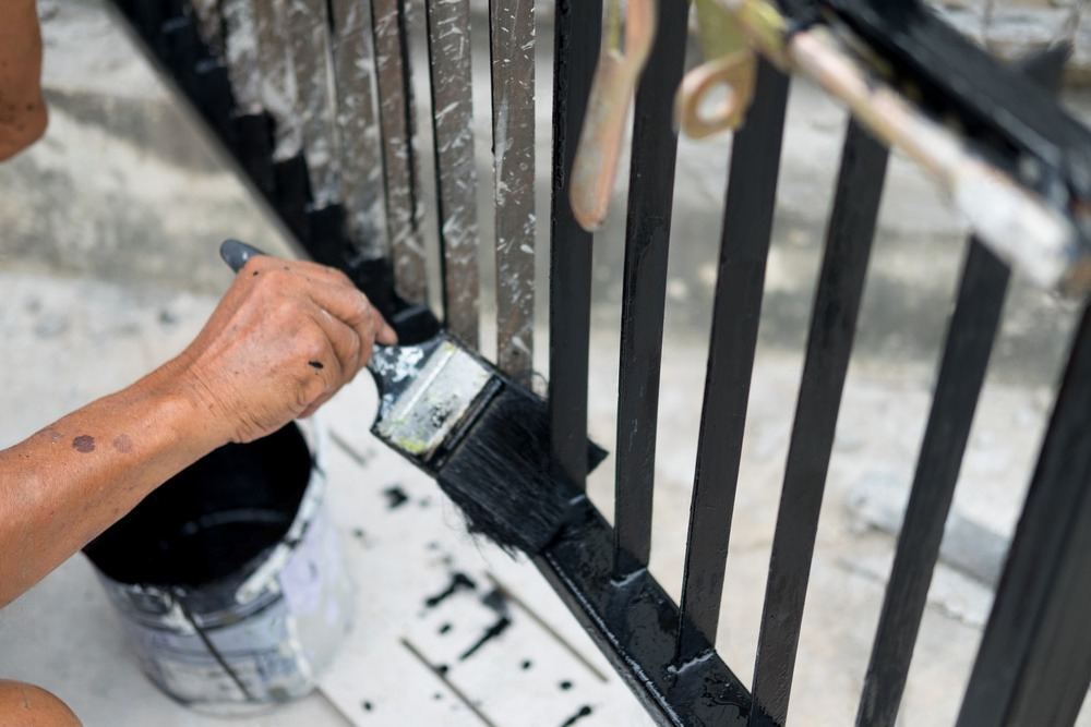 A man is painting a metal fence with a brush.