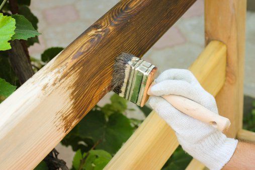 A person is painting a wooden post with a brush.