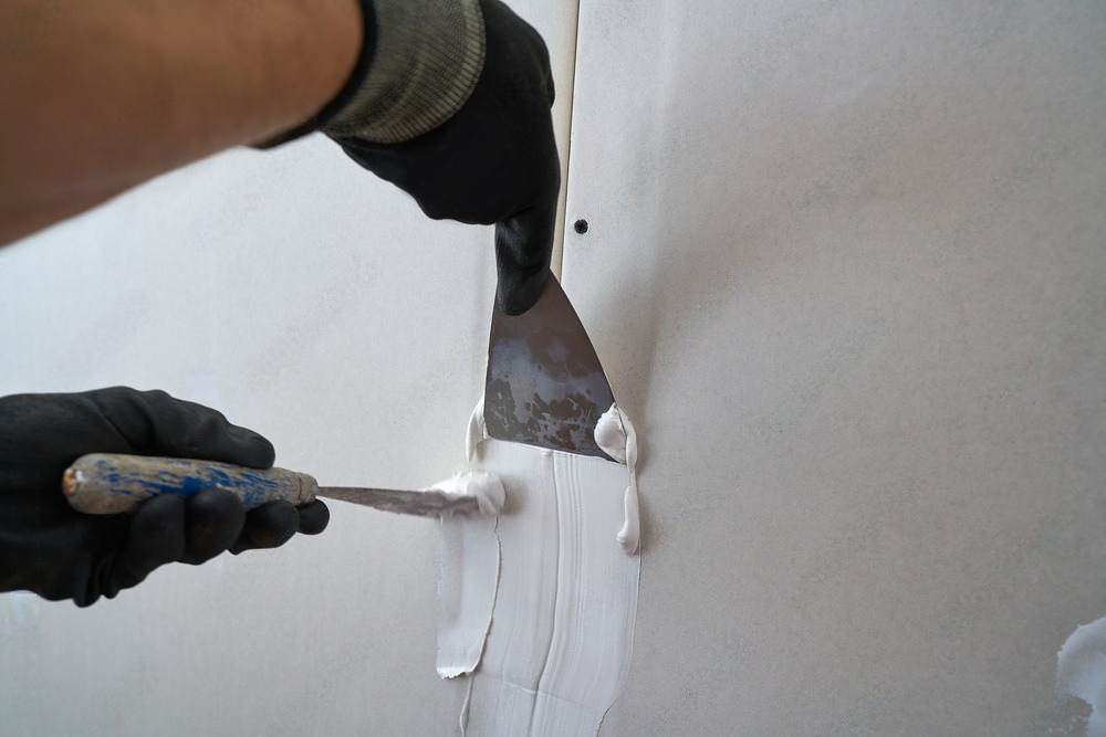 A person is using a spatula to plaster a wall.