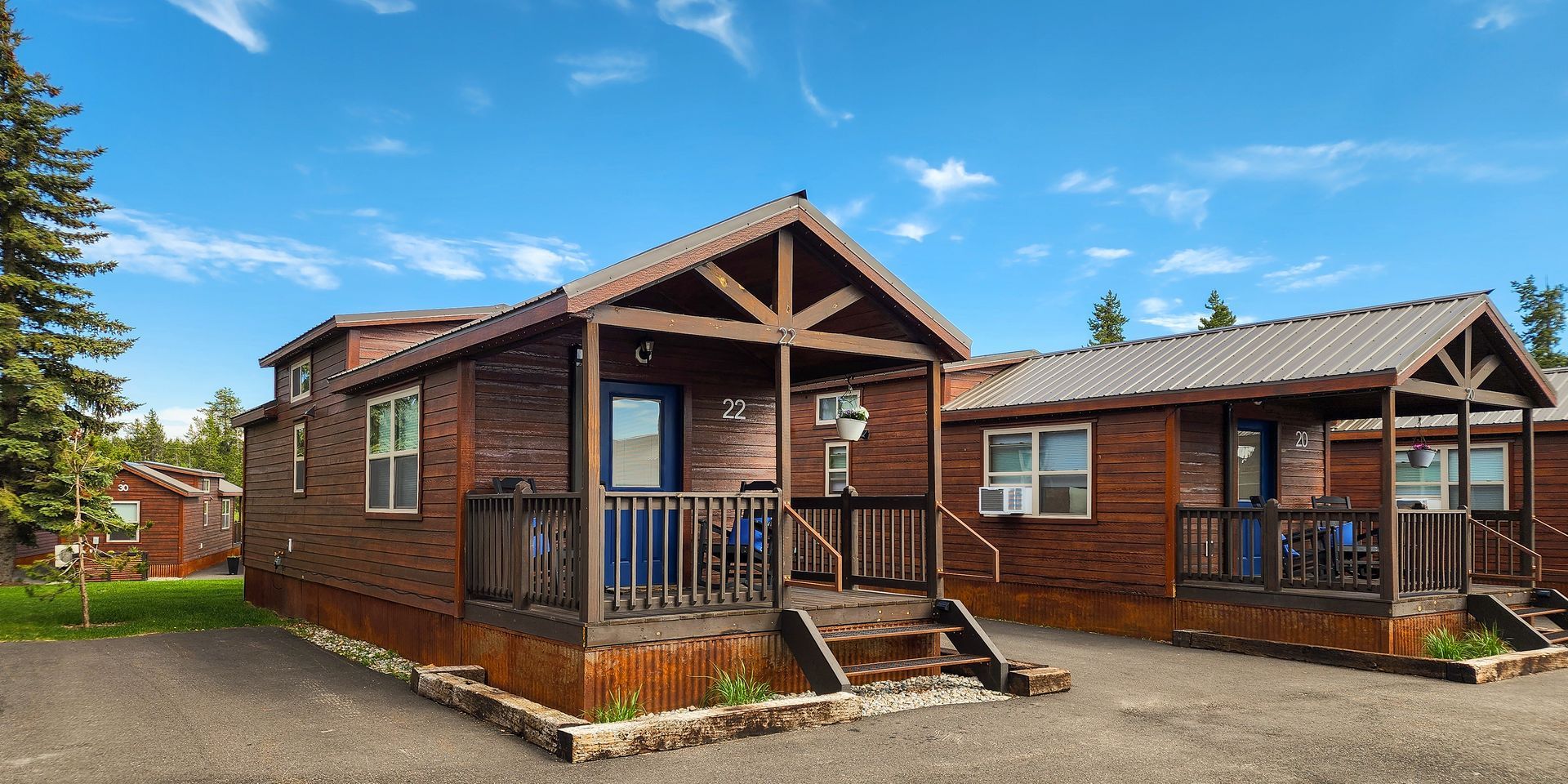 Front view of Spruce Cabin 22 with blue door, porch rocking chair, flower boxes, and corrugated metal skirting.