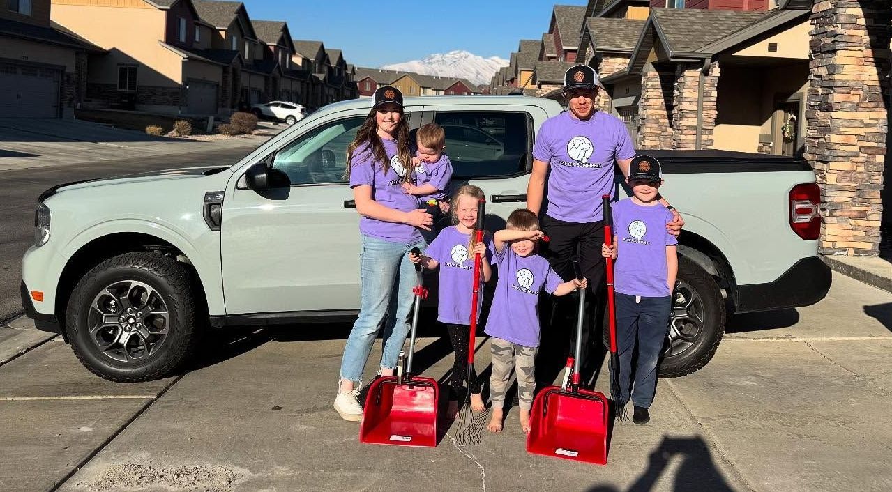 A family is standing in front of a truck holding snow shovels.