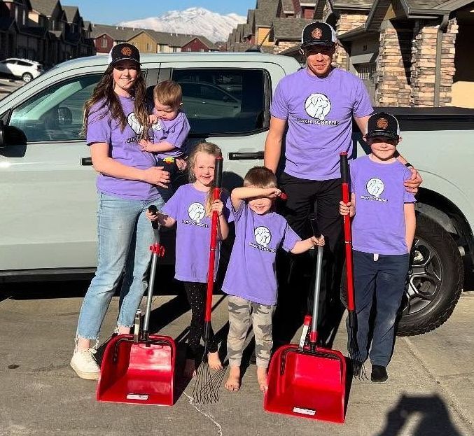 A family is standing in front of a truck holding snow shovels.