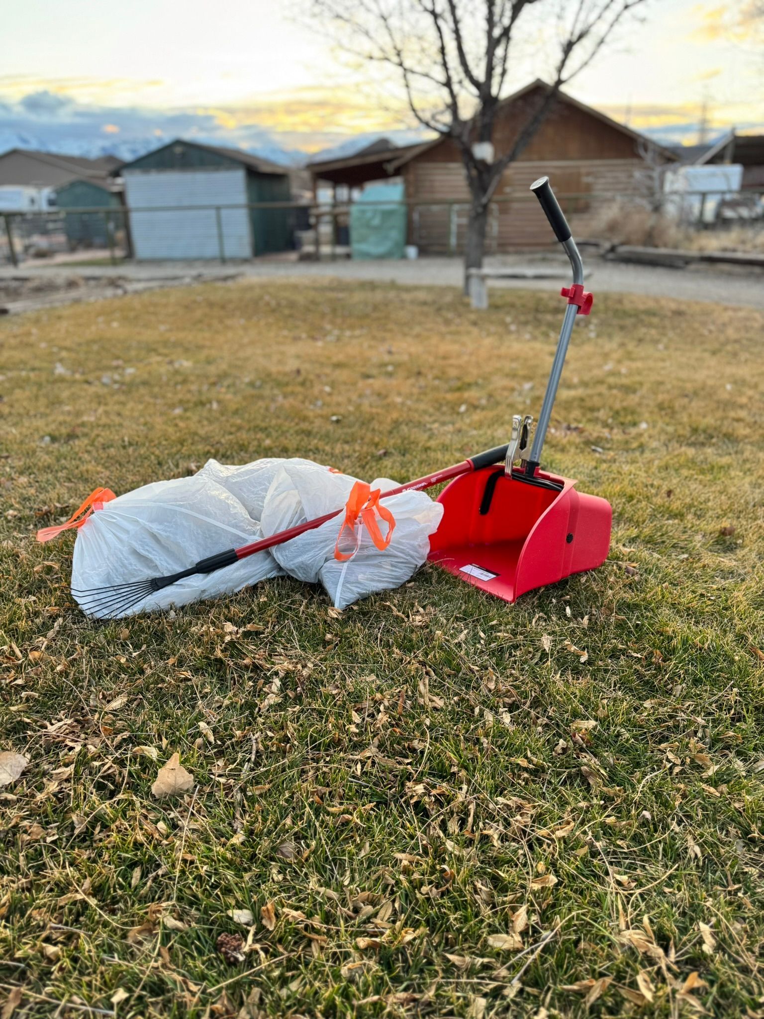 A red snow blower is sitting in the grass next to a bag of trash.
