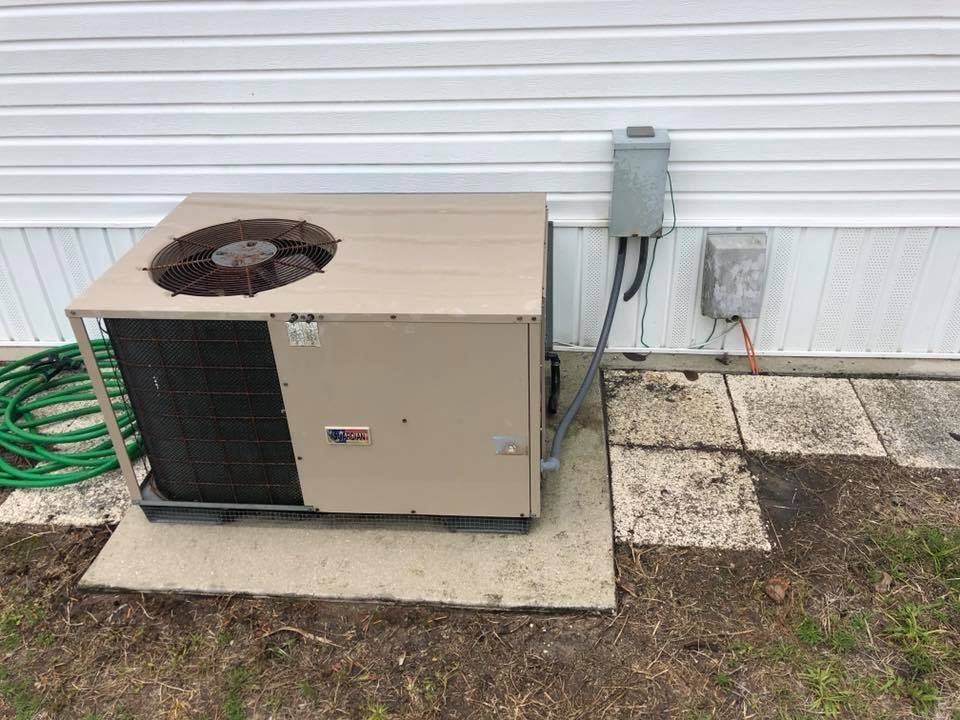 An outdoor air conditioning unit, beige in color, sits on a concrete pad next to a white house.