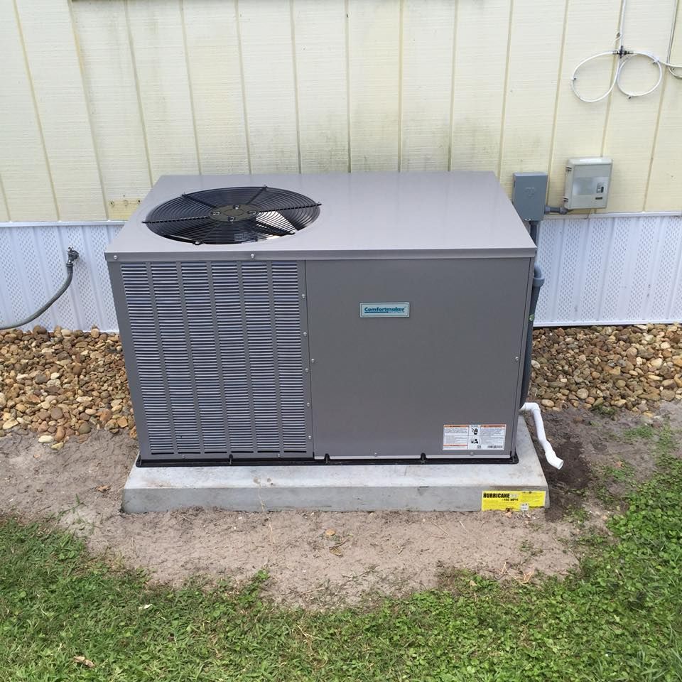 Central air conditioning unit outside a building on a concrete pad with gravel and grass.