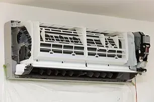 Opened air conditioning unit on a white wall, revealing internal parts and air vents.