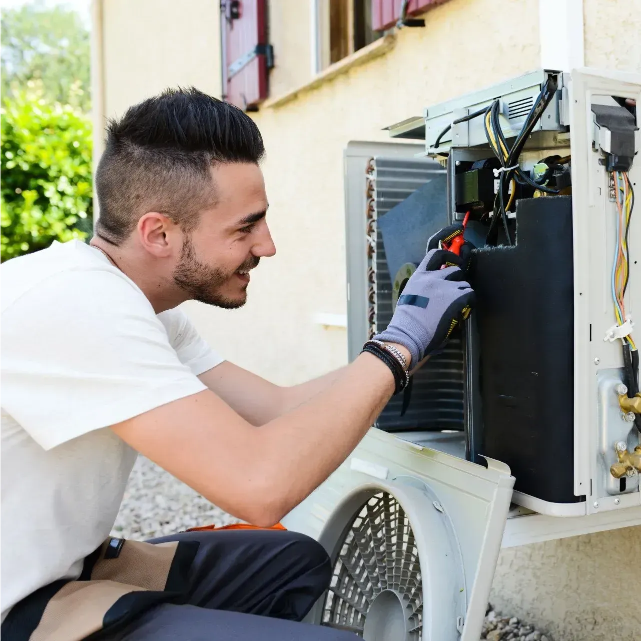 Man in work gloves repairs an outdoor air conditioner unit.