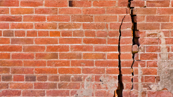 Lawn sprinkler spraying water on green grass in a yard with bushes and trees.