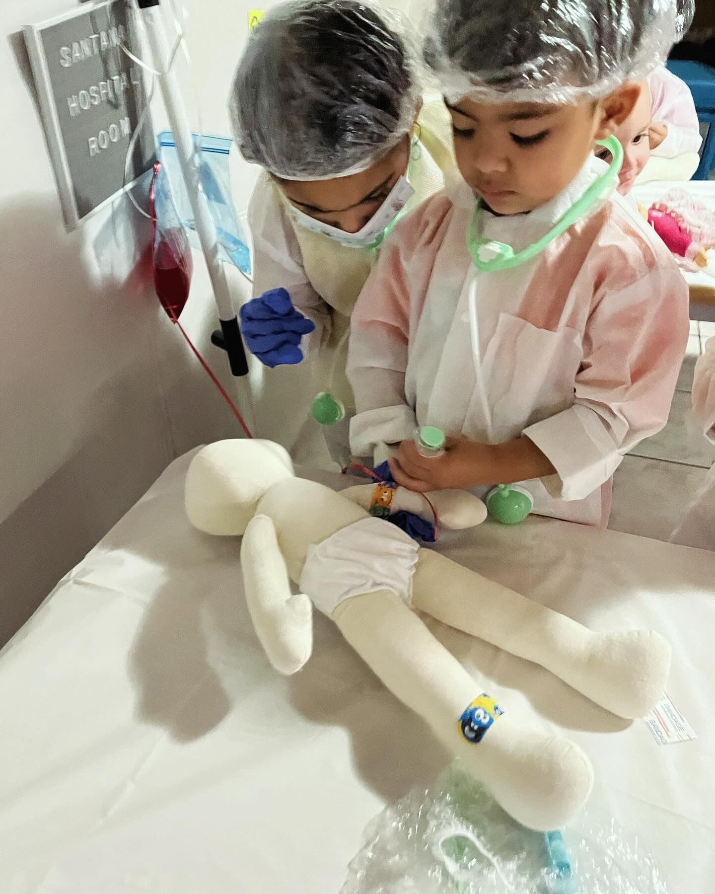 Two children dressed as doctors are playing with a stuffed animal.