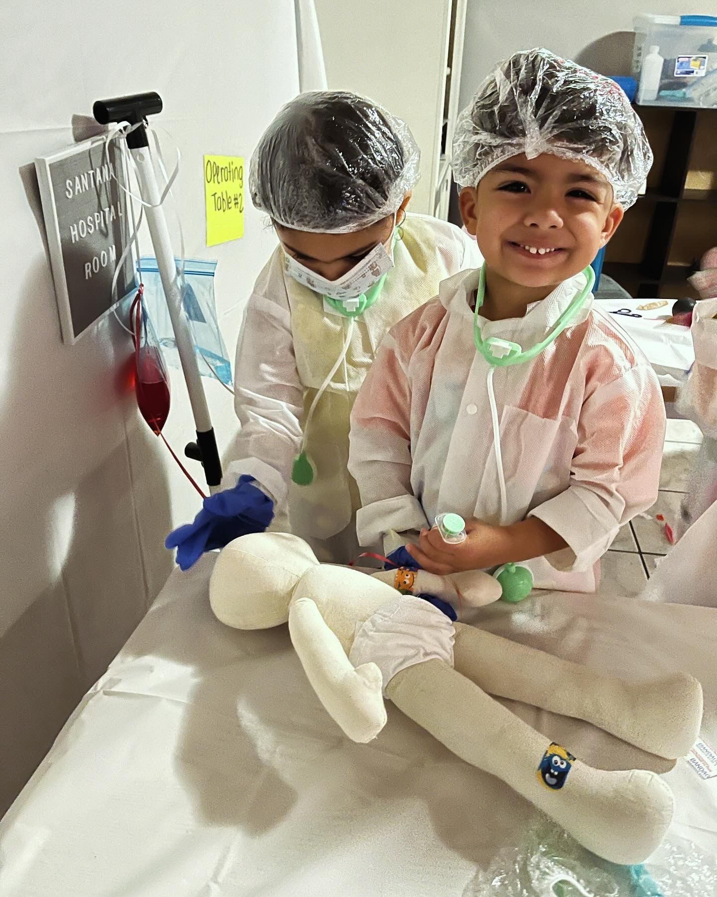 Two children dressed as doctors are playing with a stuffed animal.