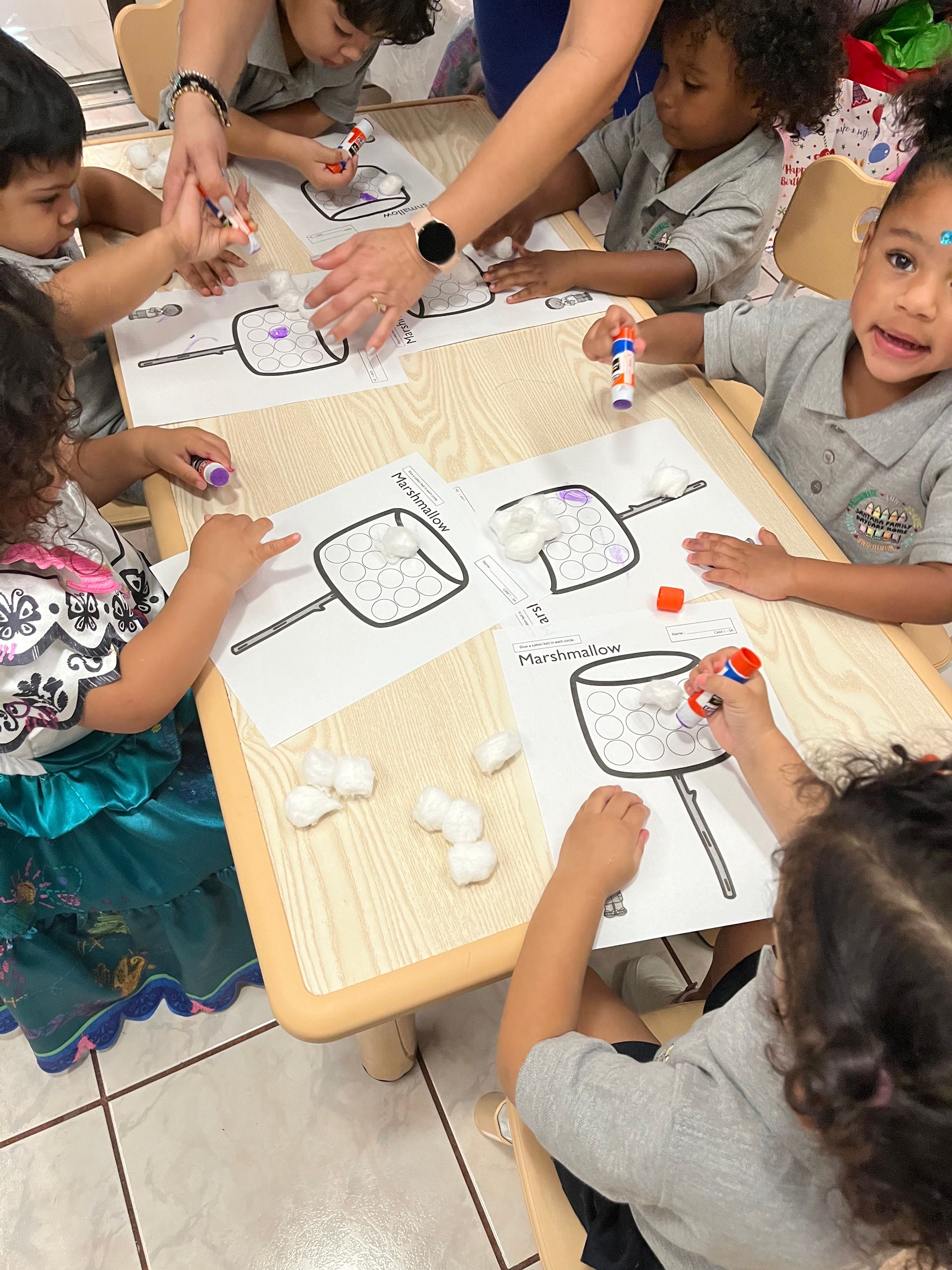 A group of children are sitting at a table drawing marshmallows.