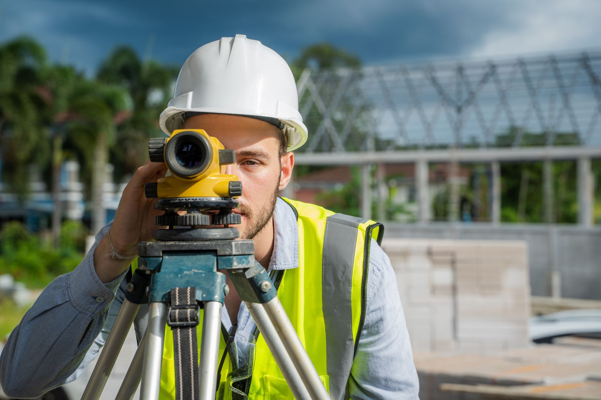 A male engineer does survey work on a construction site, while looking at the camera.