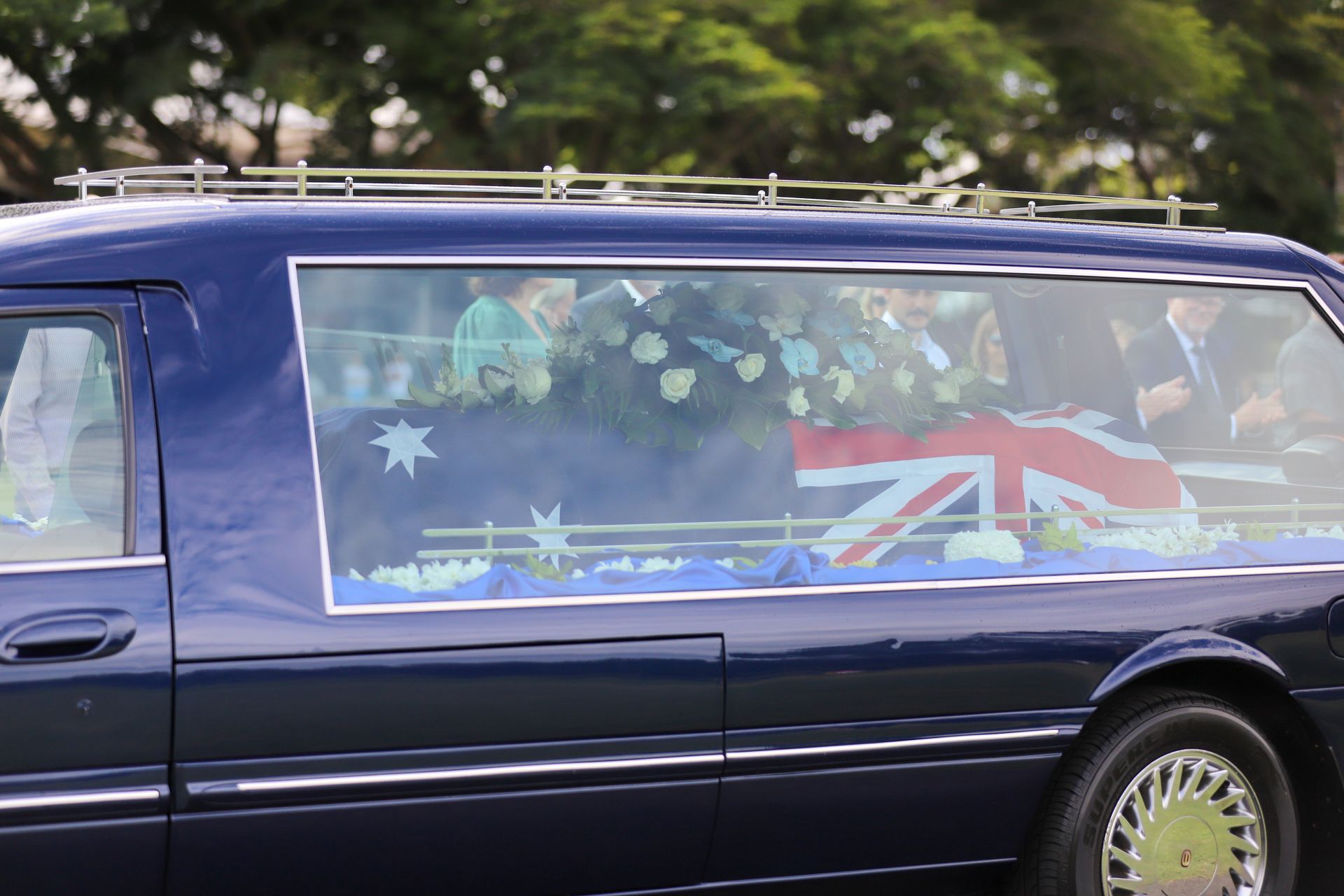 A teddy bear sits next to a basket of white roses - Funeral Services in Upper Coomera, QLD