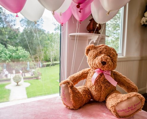A teddy bear is sitting on a table next to balloons - Funeral Services in Upper Coomera, QLD