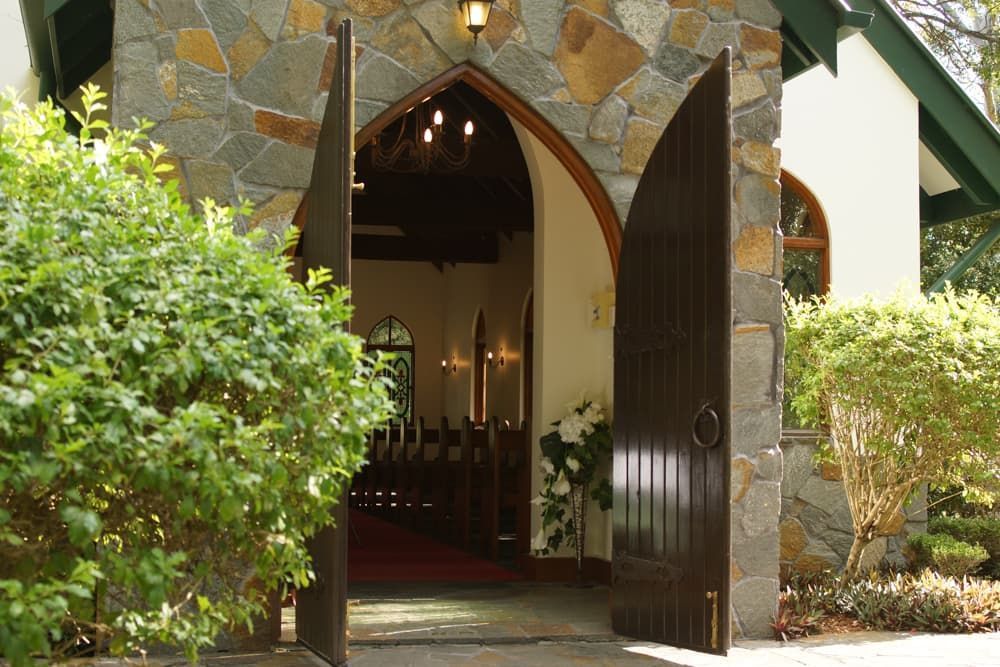 A church with the doors open and a stone wall - Funeral Services in Upper Coomera, QLD