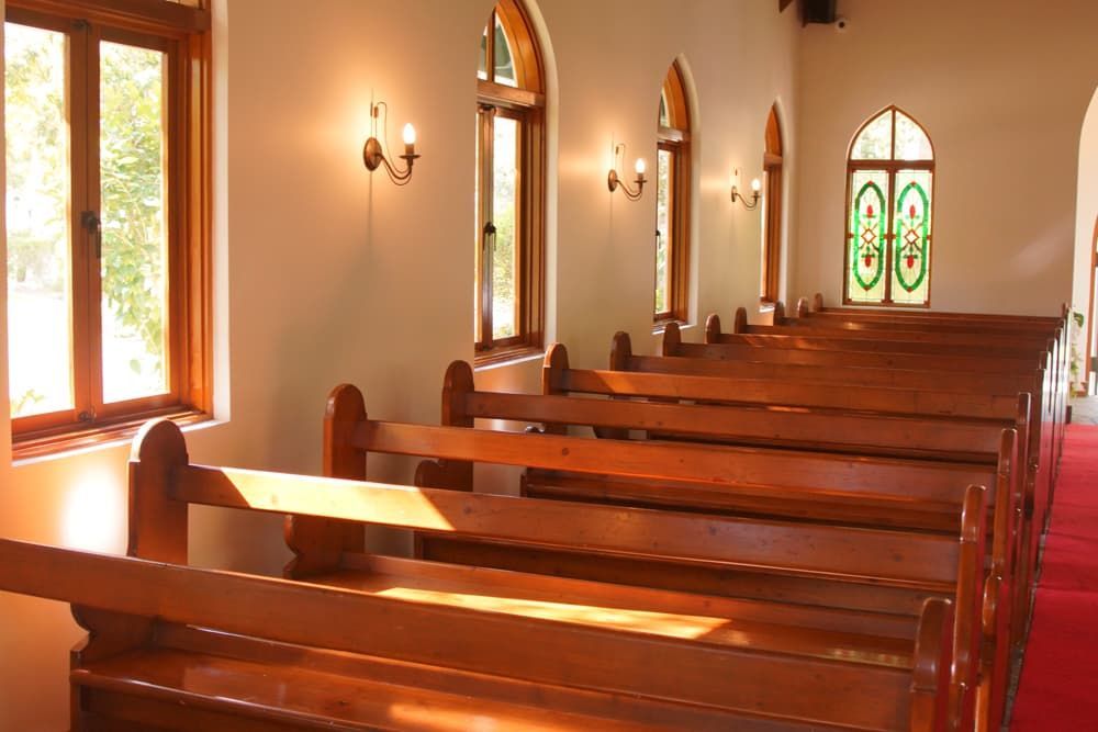 Rows of wooden benches in a church with stained glass windows - Funeral Services in Upper Coomera, QLD