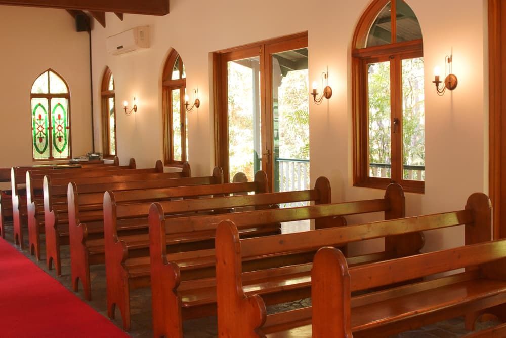 A rows of wooden benches in a church with stained glass windows - Funeral Services in Upper Coomera, QLD