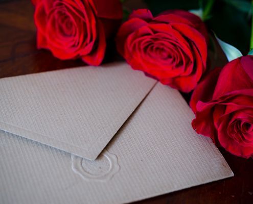 Two red roses are sitting next to an envelope on a wooden table - Funeral Services in Upper Coomera, QLD
