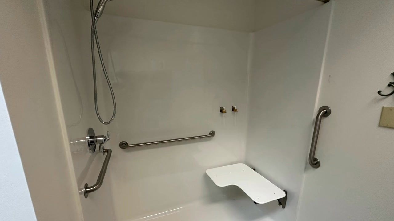 A shower with a seat and handrails and a shower head.