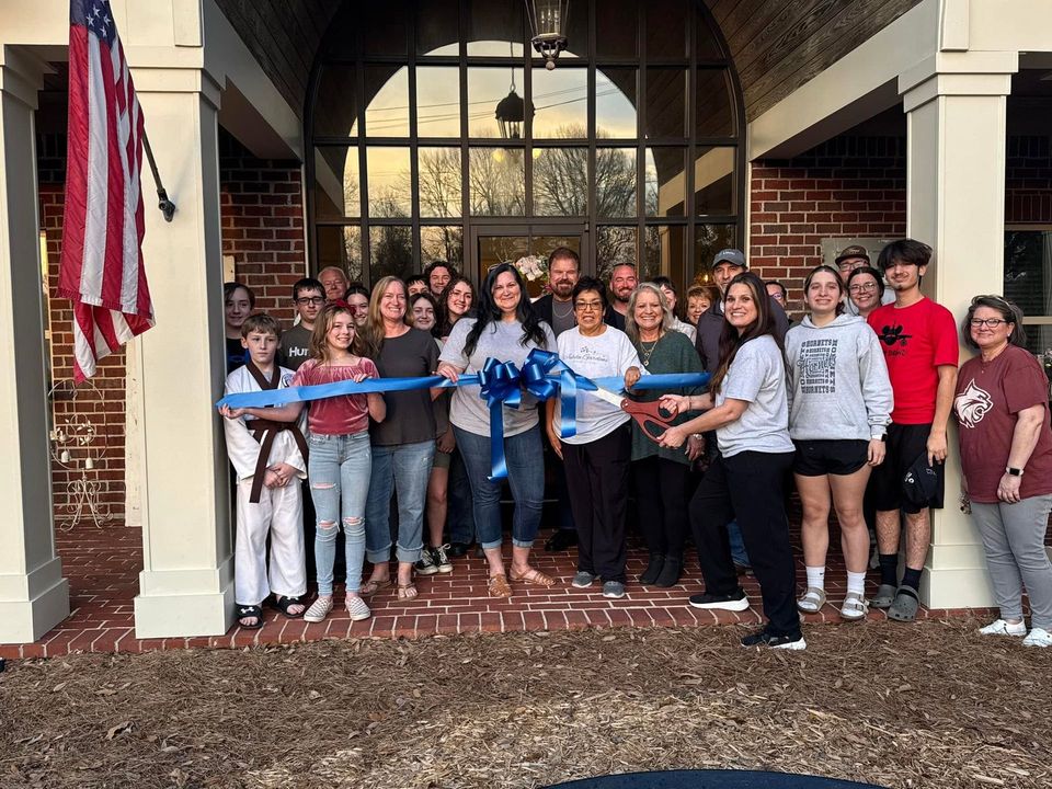 Group holding a ribbon in front of a brick building entrance with an American flag