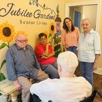 A group of people are sitting in a room with sunflowers painted on the wall.