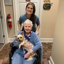 An elderly woman in a wheelchair is holding a small dog.