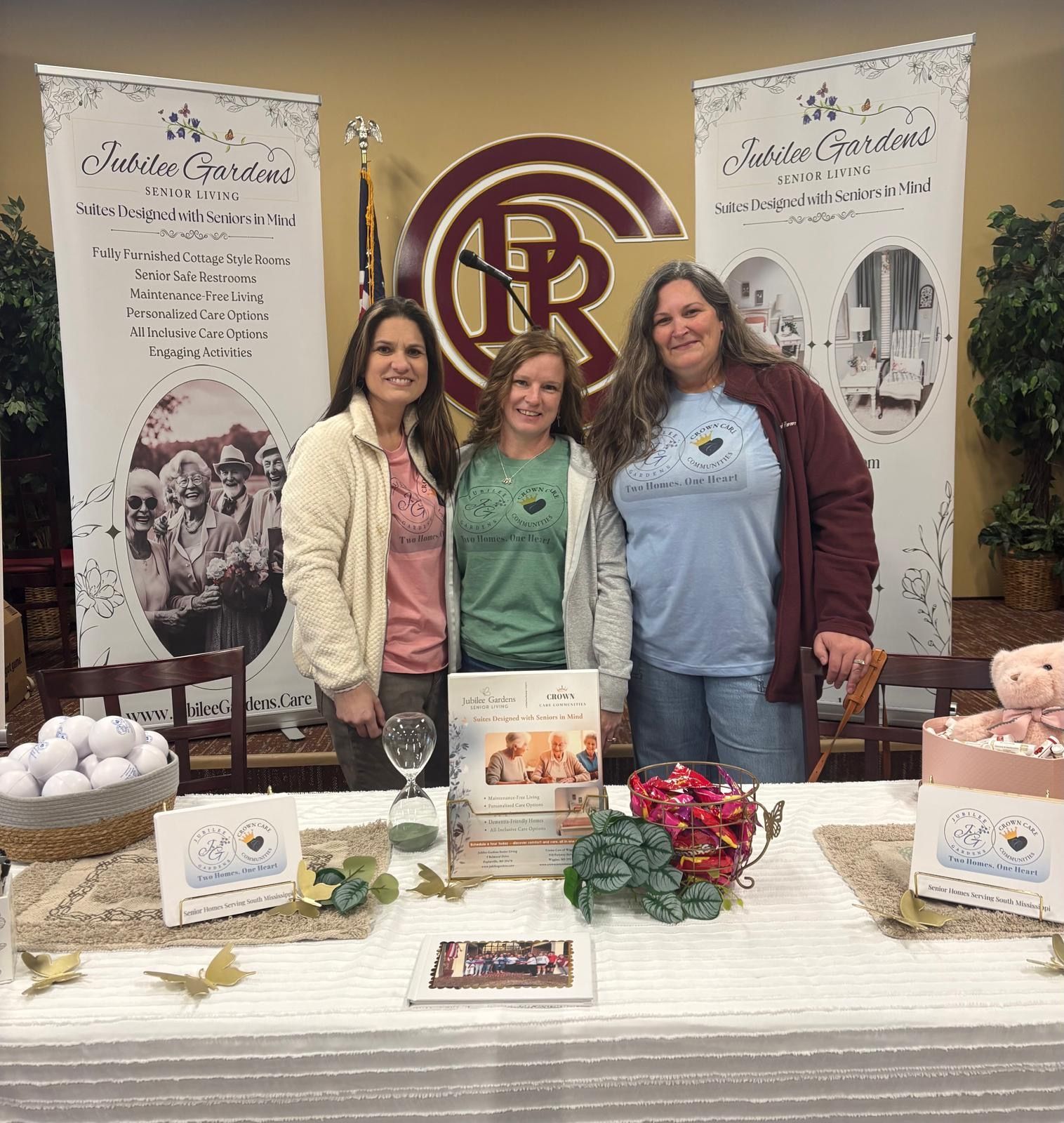 Three women stand behind a table with branding for 