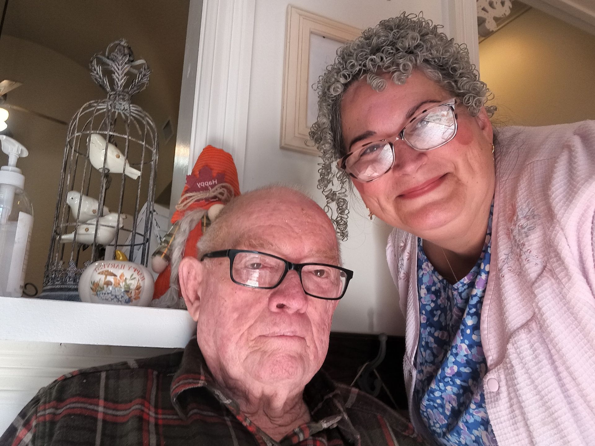 A selfie of two people smiling together indoors near a decorative birdcage and a small gnome.