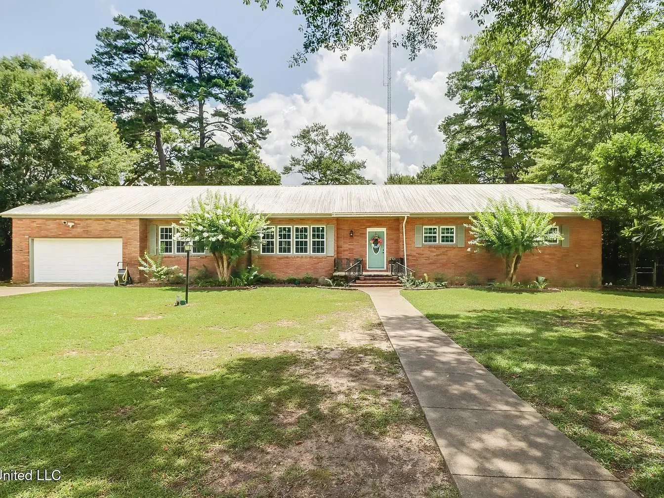 A single-story ranch-style brick house with a white garage door, light-colored roof, and a sidewalk leading to the door.