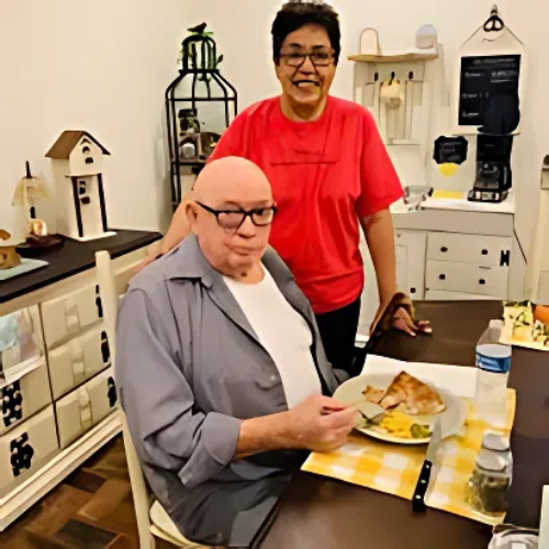 A man sitting at a table with a plate of food and a woman standing behind him