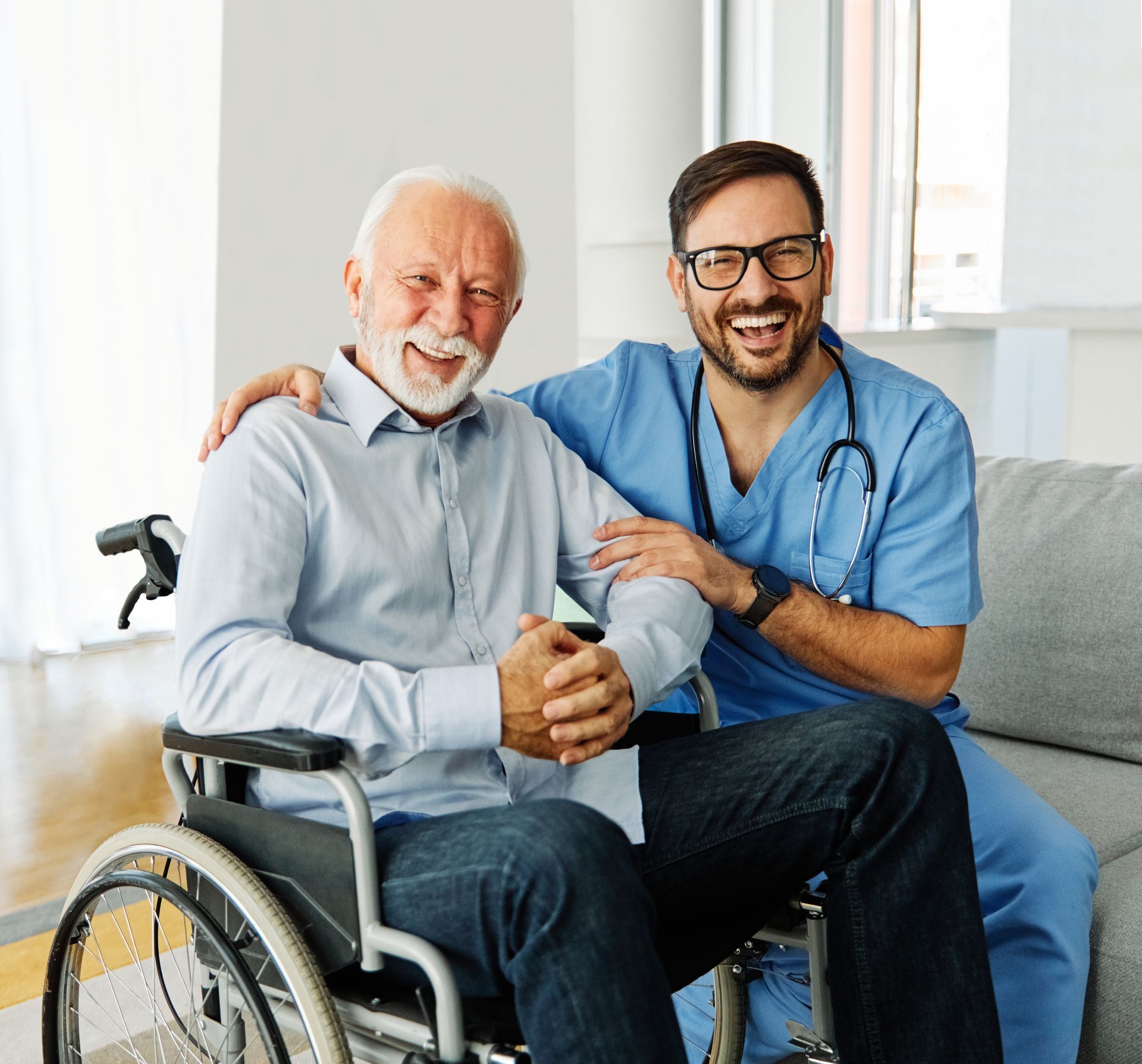 A nurse is sitting on a couch next to an older man in a wheelchair.