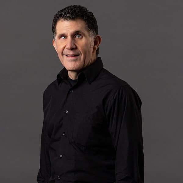 Man in black shirt, looking at the camera, against a grey backdrop.