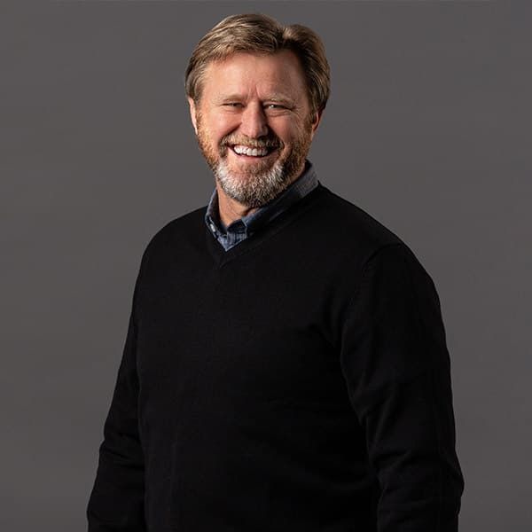 Man in black shirt, looking at the camera, against a grey backdrop.