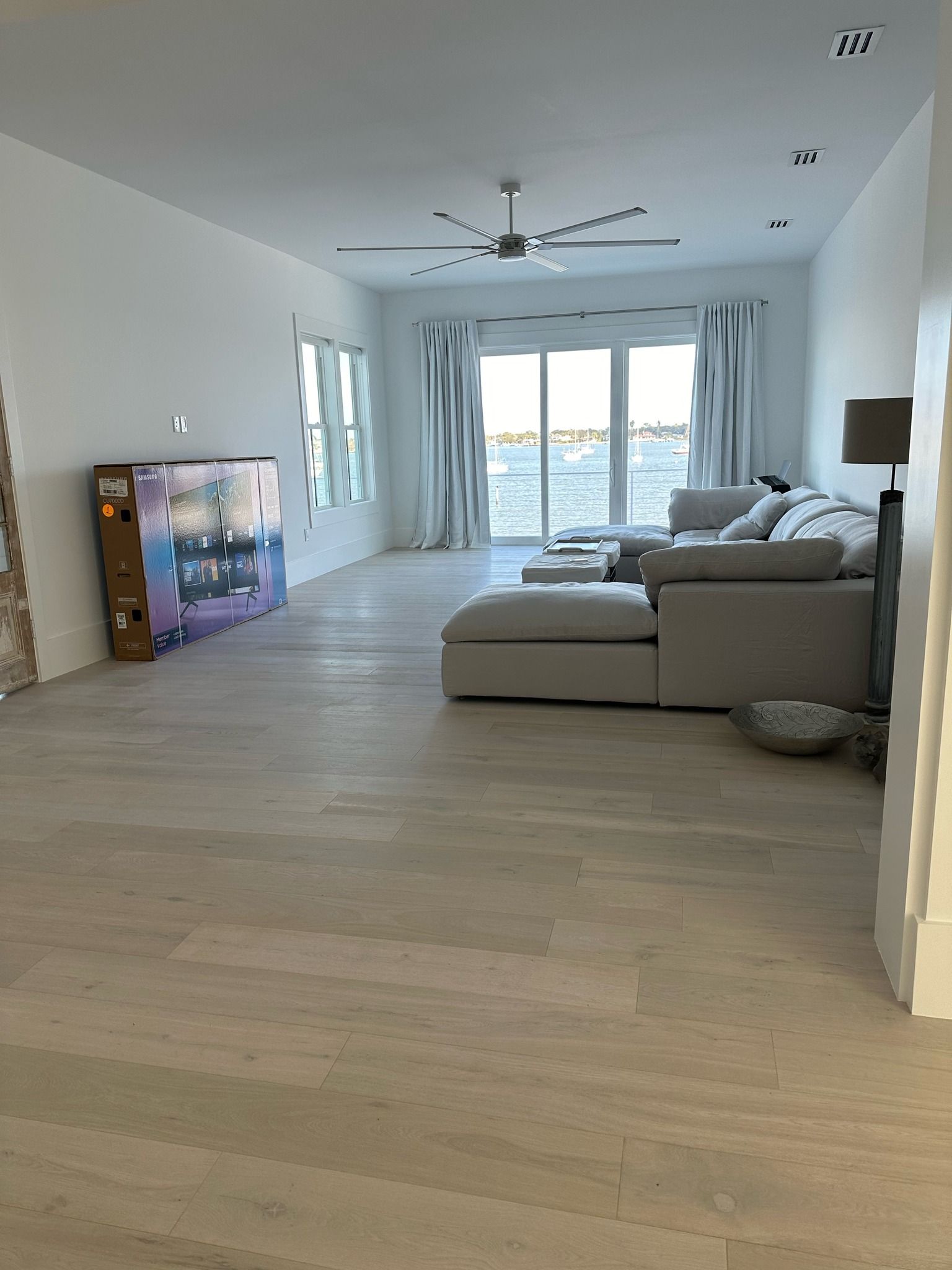 Spacious living room with light wood floors, sectional sofa, and water view through sliding glass doors.