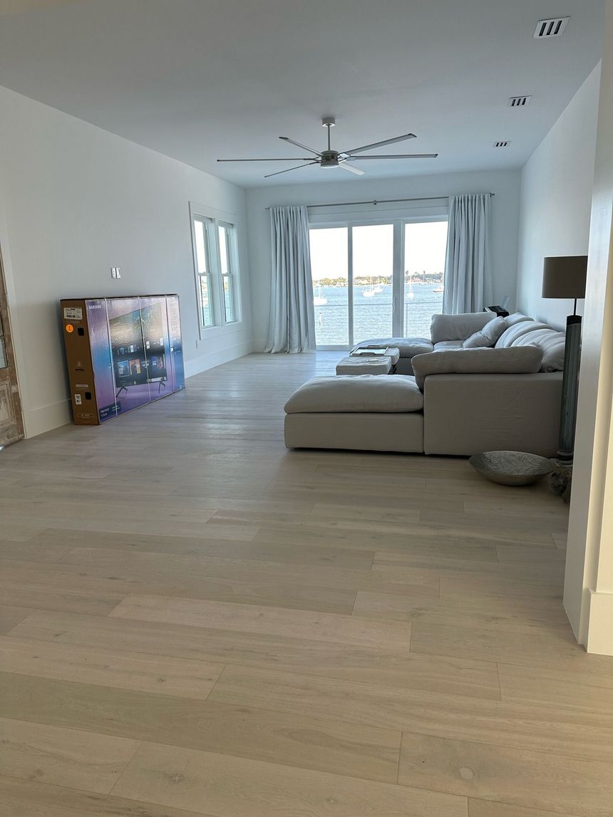 Spacious living room with light wood floors, sectional sofa, and water view through sliding glass doors.