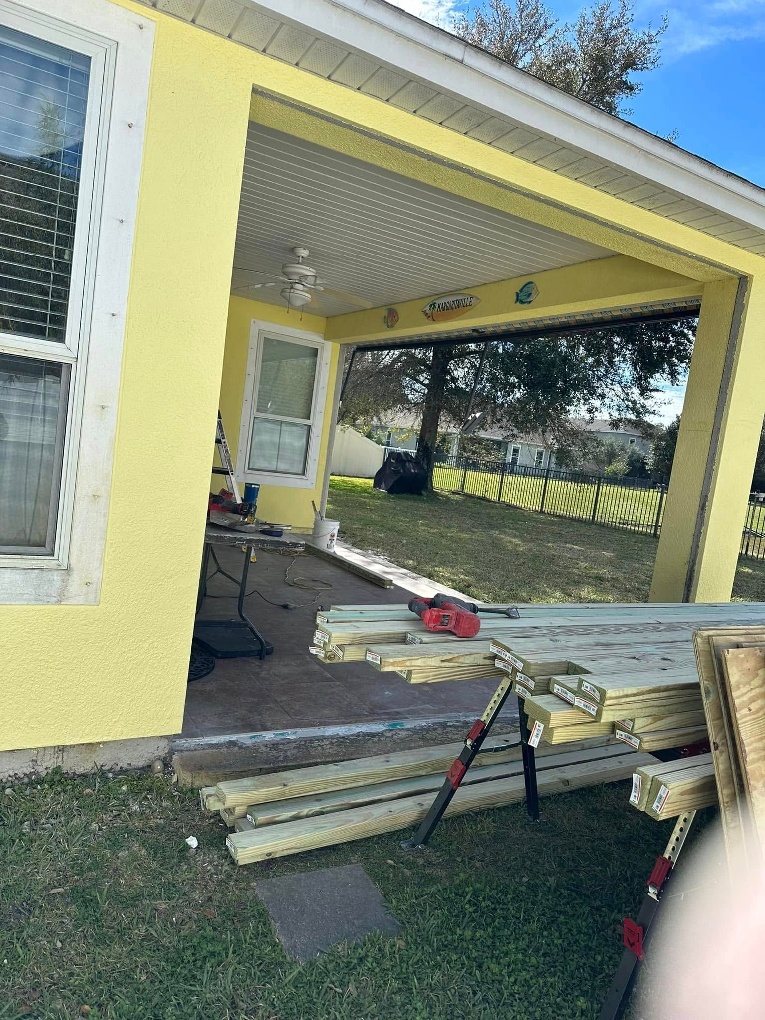 Yellow house exterior with a covered porch under construction; tools, lumber on the ground.