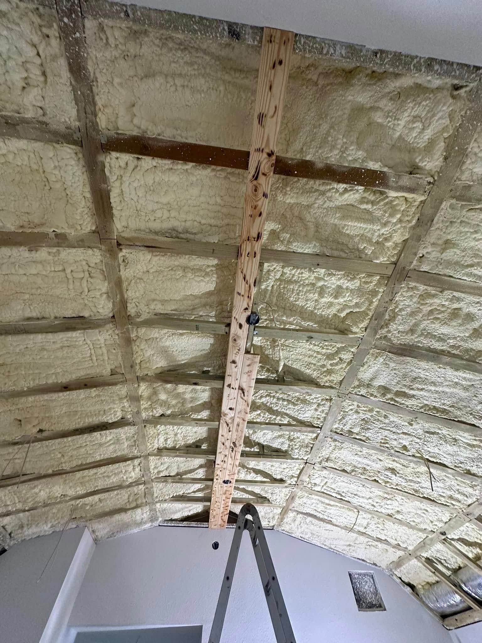 A ceiling with foam insulation, a wooden beam, and a ladder are visible.