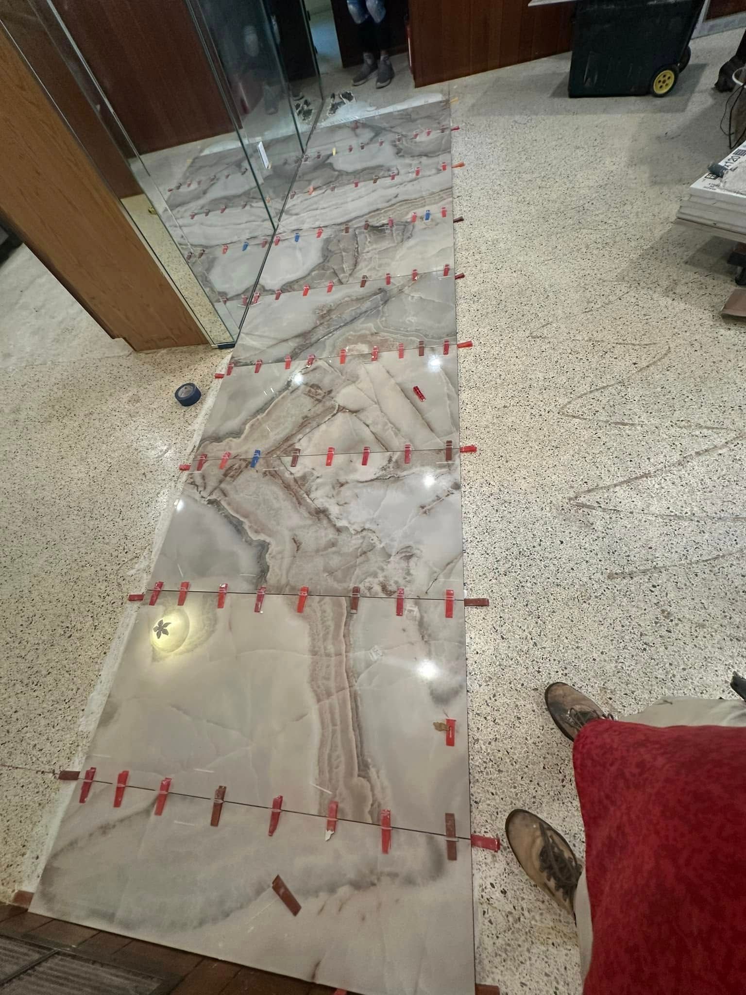 Large tiles are being installed on the floor, using red leveling clips.