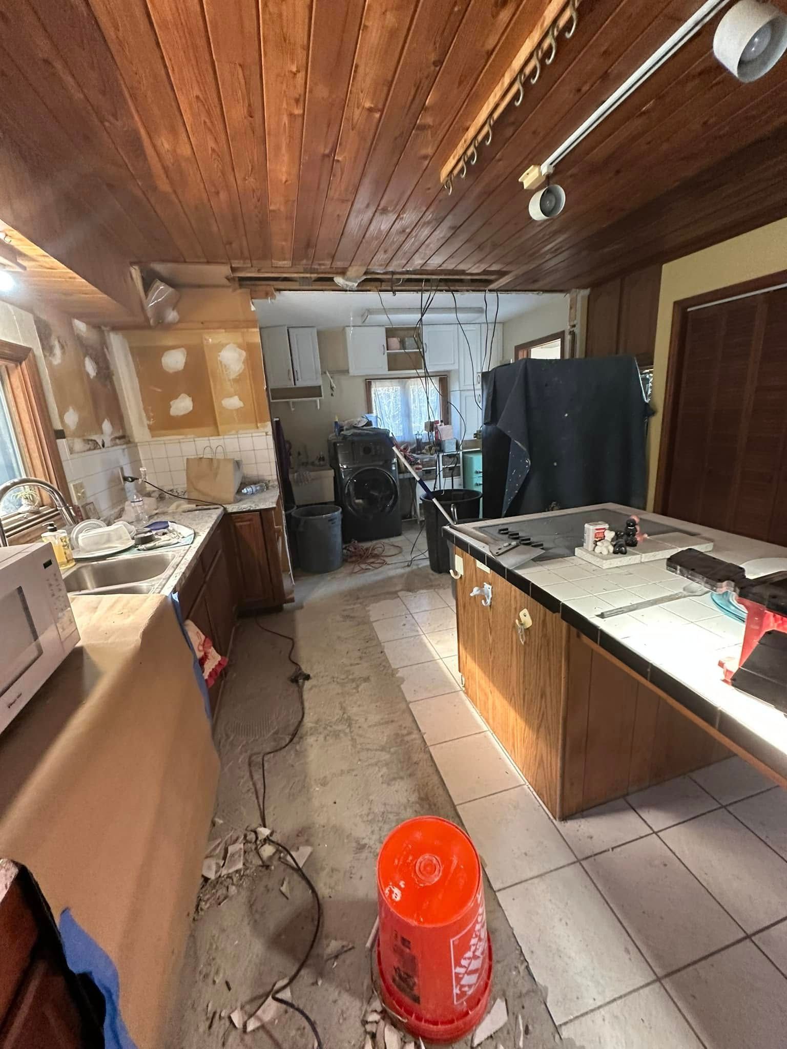 Kitchen demolition in progress; cabinets removed, debris on floor, red bucket.