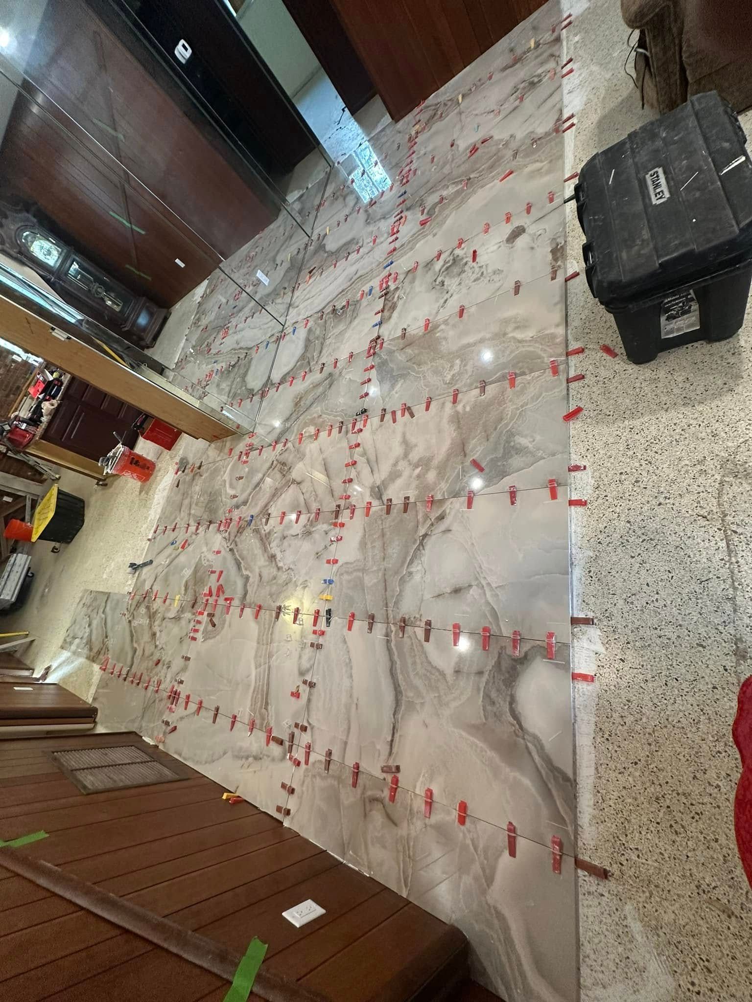 Large-format marble tiles being installed on a wall, red leveling clips used throughout.