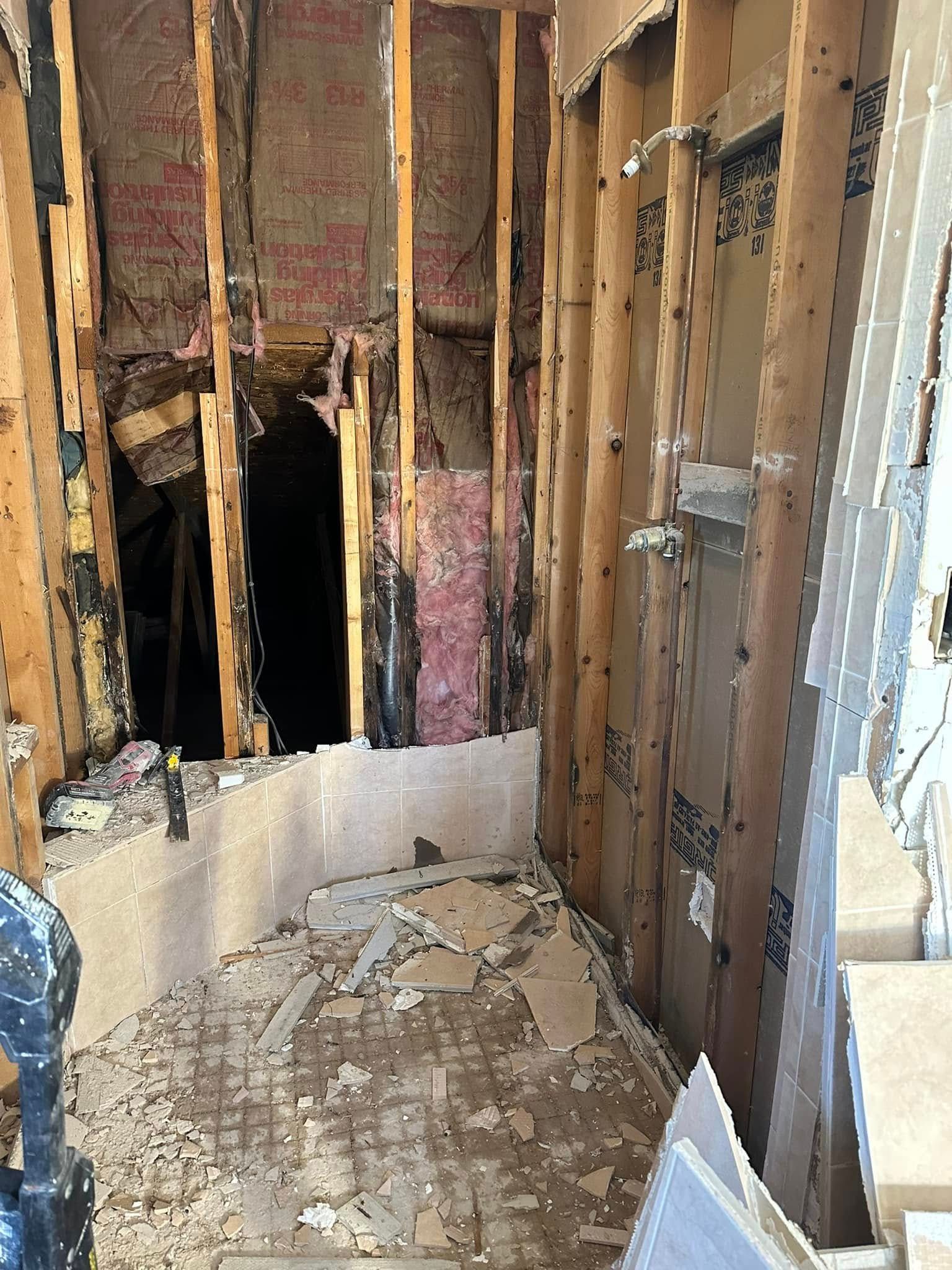 Bathroom demolition: exposed studs, damaged walls, debris on floor, dark opening.