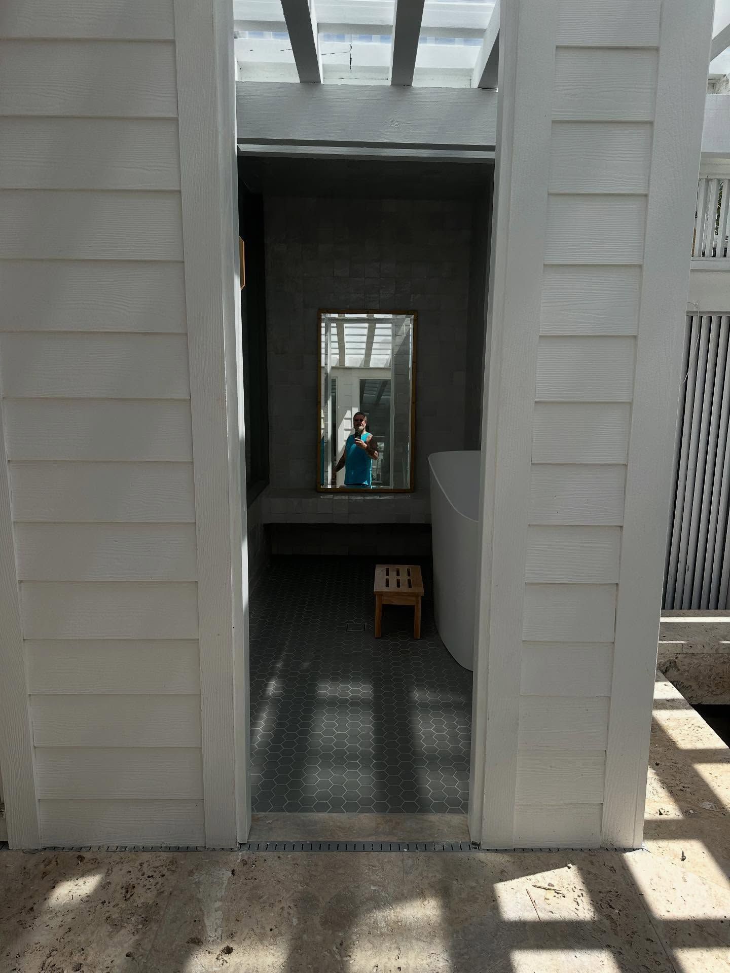 White-walled opening to a room with a mirror and a person reflected; sunlight streams from above.