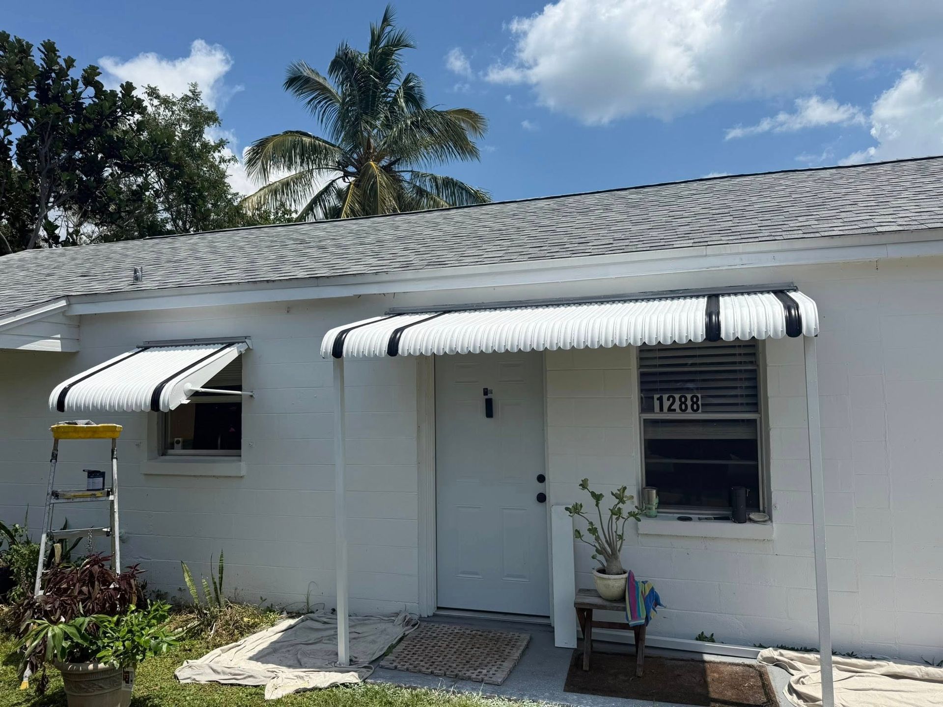 White house with striped awnings, doorway, and windows under a blue sky.