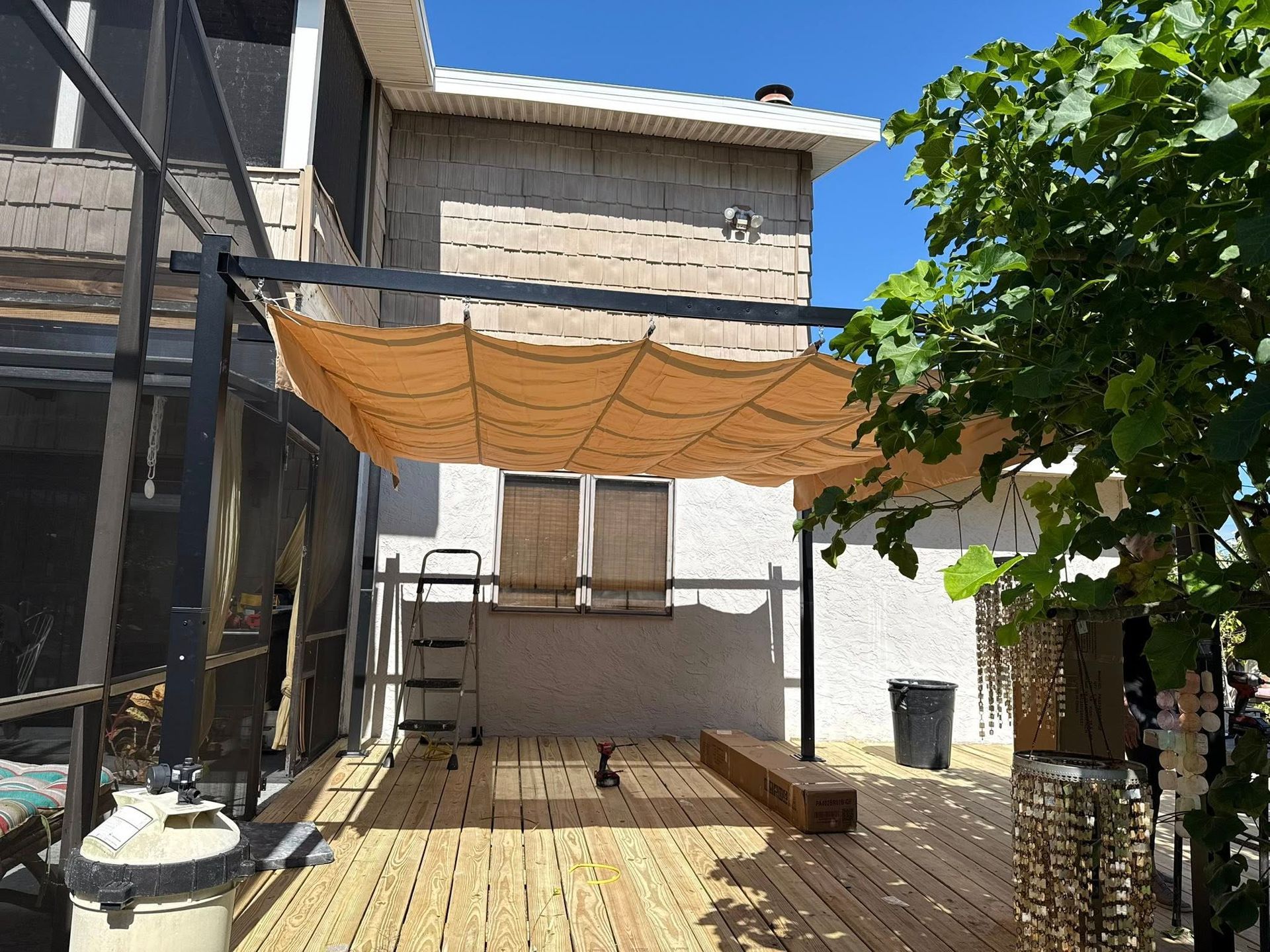 Wooden deck with shade canopy, small dog, and part of a house.