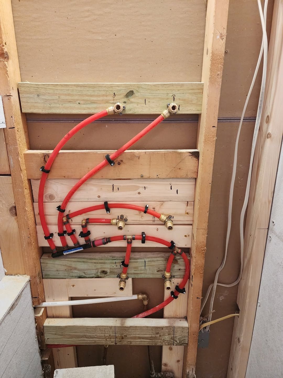 Red PEX plumbing pipes and brass fittings installed in a wood-framed wall.