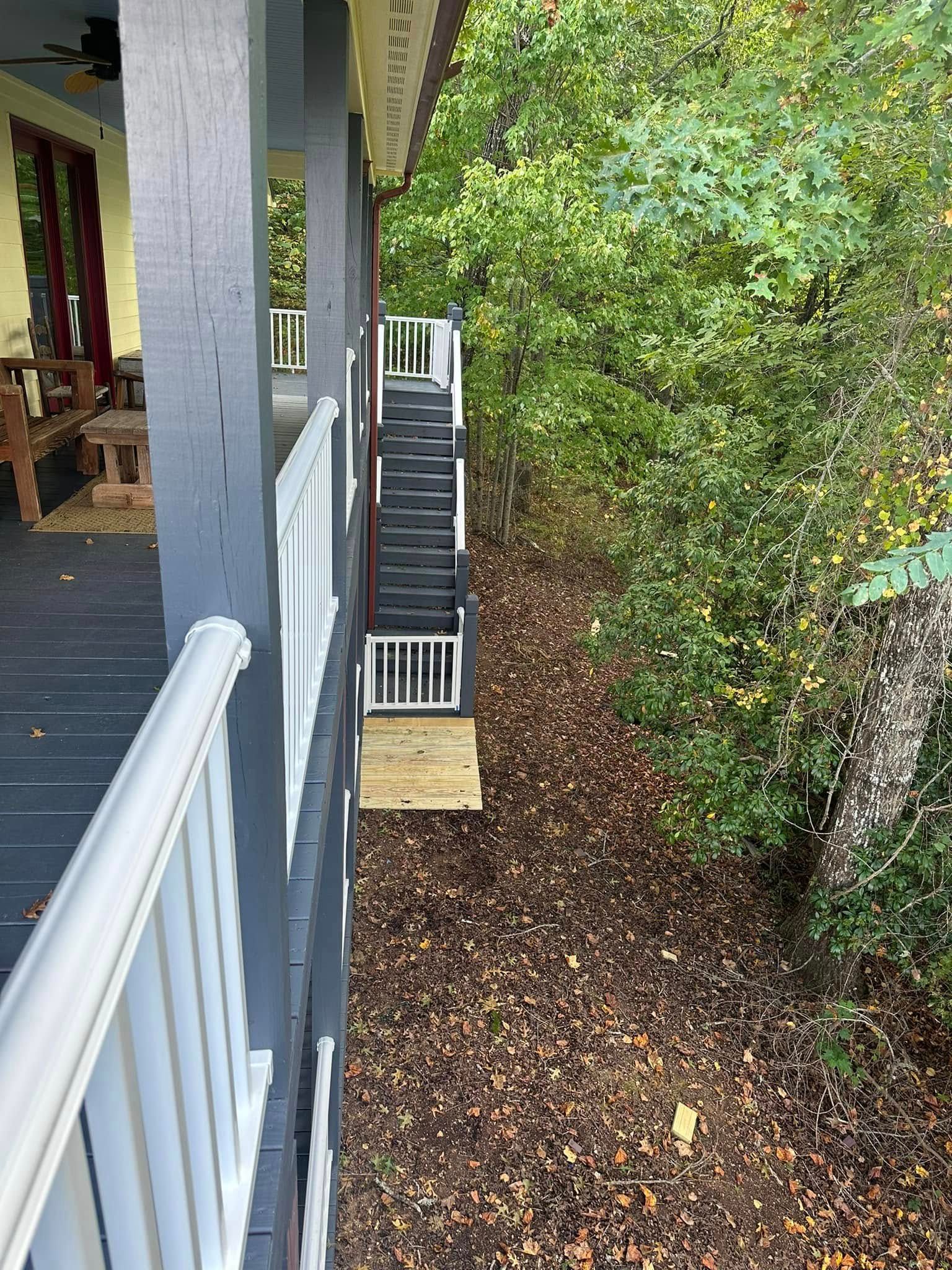 A wooden porch with white railing, stairs, and a forest.