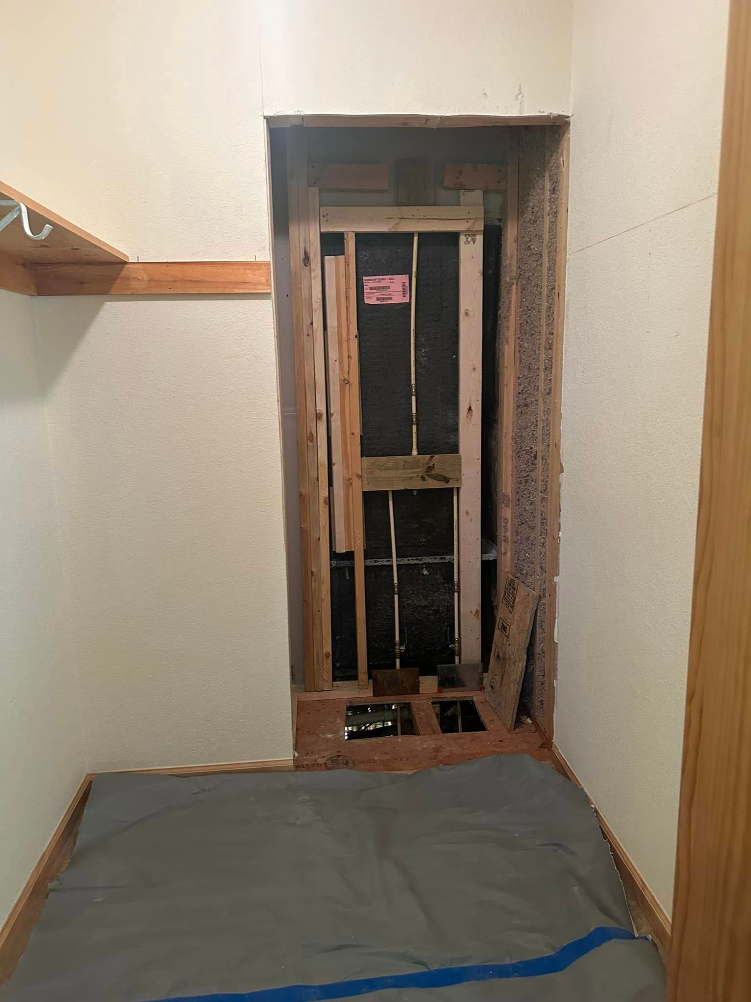 A closet doorway with exposed framing and insulation, damaged lower portion, and protective tarp on floor.